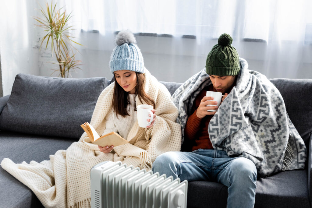 Young couple bundled up in blankets on the couch near a heater