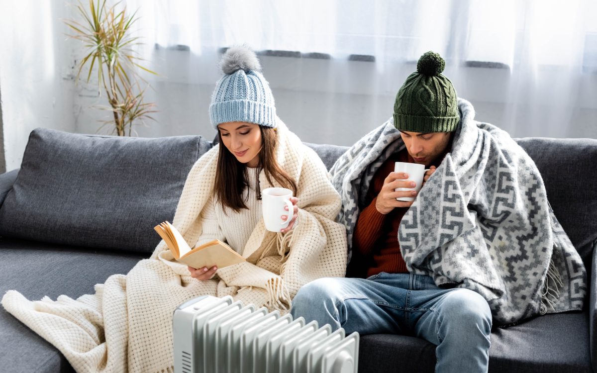 Young couple bundled up in blankets on the couch near a heater