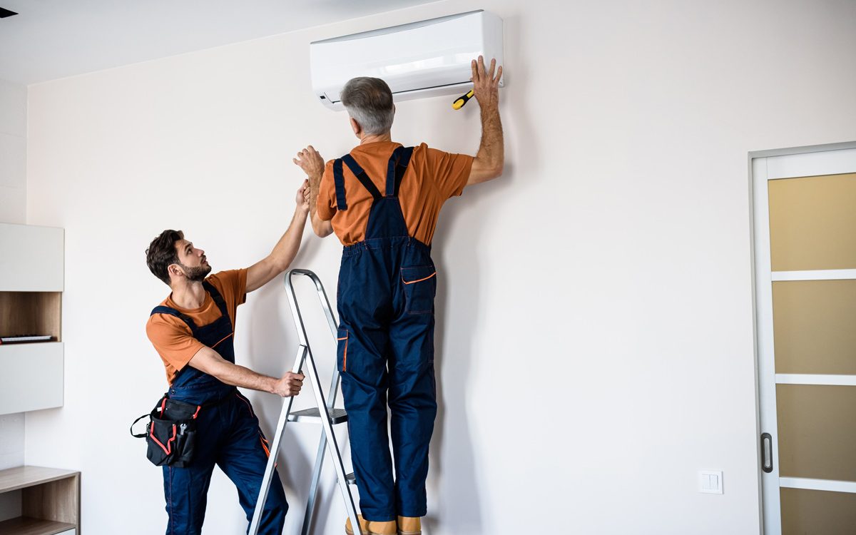 Two professionals in orange shirts installing an AC unit on the wall of a North Fort Myers home.